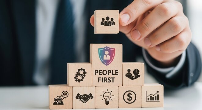 A hand places a wooden block with people icon on a 'people first' business strategy pyramid