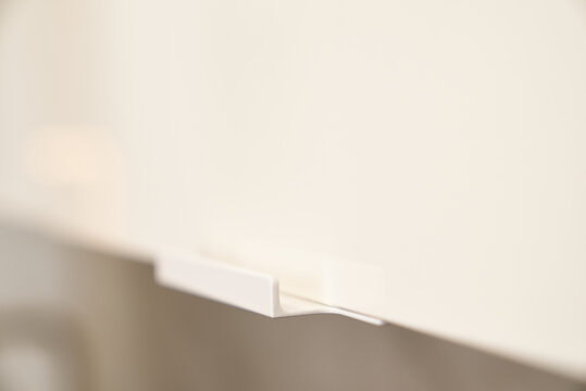 A minimalist white chest of drawers handle, a detail of a modern interior.