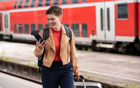 Woman with suitcase using mobile phone at train station platform