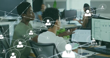 Pointing Korean colleague guiding peer at monitors in open office in business-casual, showing UI © vectorfusionart