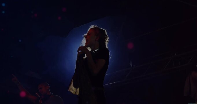 Lead singer leaning forward holding mic onstage, whipping hair, halo flaring, engaging music crowd
