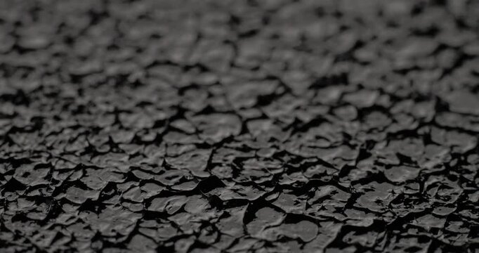 Macro Cracked Mud Texture on Black. Slow panning footage across a fissured dark surface, showcasing intricate polygonal crack patterns and rough granular details under subtle directional lighting.