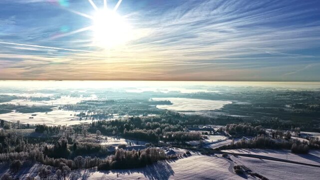 Bright winter aerial with low sparkling daze sun above snowy landscape and layered clouds, forest backdrop background