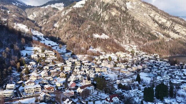Aerial winter panorama of Walensee village with snow-covered houses, winding streets, and steep alpine mountainsides.