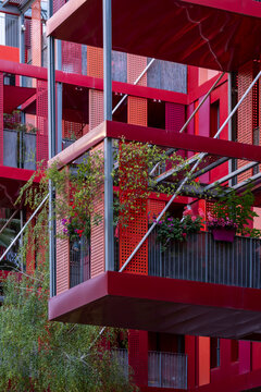 Modern residential architecture features a red facade balcony and plants in Port Marianne Montpellier France photographed in bright daylight