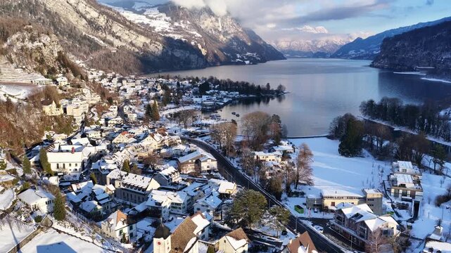 Aerial winter view of lakeside village on Walensee with snow-covered rooftops, church tower, and alpine mountains.