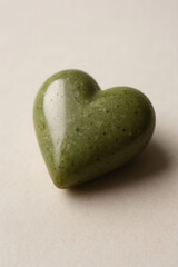 Small green heart shape made from natural material on a light surface showing texture and design