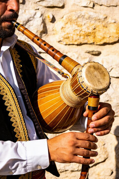 Man playing traditional reed instrument and frame drum in embroidered vest. Assyrian New Year cultural music performance. Ethnic folk heritage and festival celebration tradition. portrait format
