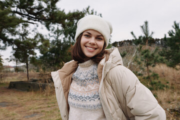 Obraz premium Smiling woman wearing a beige puffer coat and patterned knit sweater outdoors in a chilly landscape with trees and open space.