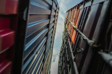 Naklejka premium Low angle perspective of cargo containers forming corridor toward sky, abstract industrial composition, logistics network concept, freight transportation, container terminal, modern global commerce ba