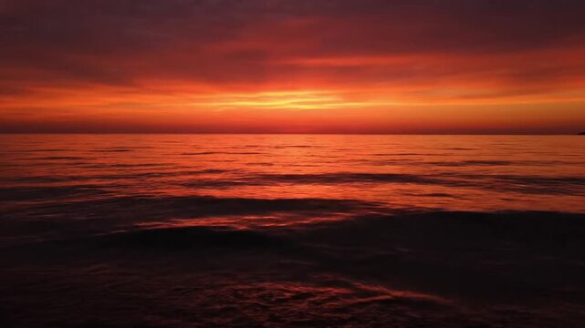 Serene ocean sunset with vibrant red, orange, and purple hues reflecting across calm rippling waves, creating a tranquil and breathtaking seascape that evokes peace, natural beauty
