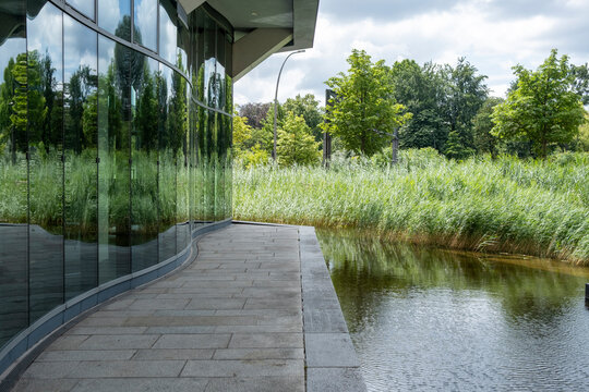 Modern urban architecture by pond wetland with glass reflection and walkway in landscape showing sustainability ecology and calm water design