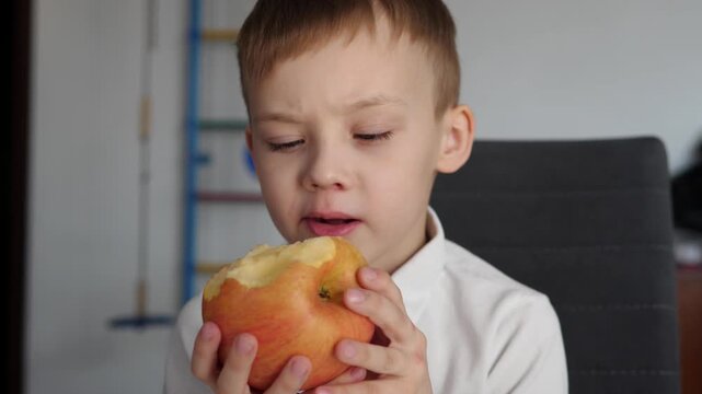 Cute boy eating a fresh red apple at home. Healthy snack and natural nutrition concept. 