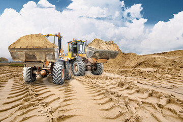 Heavy equipment is at work at the construction site, with two loaders transporting sand in buckets....