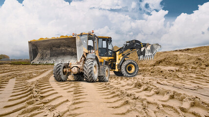 Obraz premium Deep tracks from machinery leave imprints on the sandy ground where two heavy loaders work under a cloudy sky. Rental equipment at a construction site