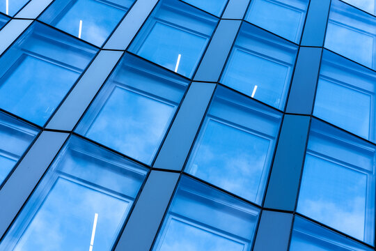 Blue modern architecture glass facade with reflections and windows forming an abstract geometry pattern for a clean contemporary corporate exterior