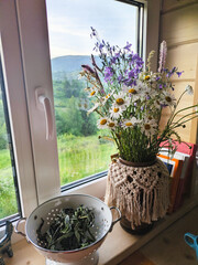 A vase with a bouquet of wildflowers and daisies on a windowsill