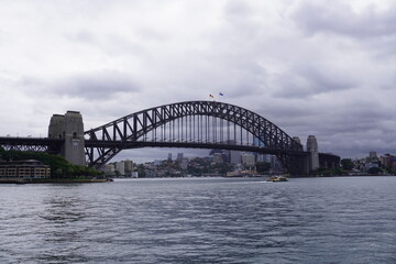 Obraz premium Sydney Harbour Bridge spanning across calm harbour water under overcast cloudy sky 
