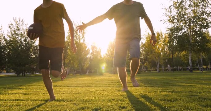 Cheerful dad and son run barefoot on green grass. Laughing dad enjoys summer weekend with boy. Loving father bonds with kid at sunset. Happy childhood and parenting lifestyle. Dad and child