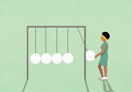 Young woman holding ball of large Newton's cradle against green background