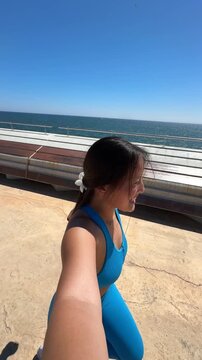 Happy asian woman jogging takes a selfie video at the seaport