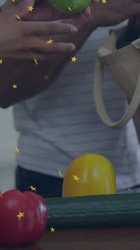 Vertical video: Couple reaching, passing produce, packing grocery tote as gold stars guide