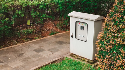 Industrial electrical panel next to sidewalk with lush green bush and grass wallpaper background