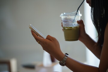 Title: Young woman using a smartphone and holding a cold beverage in a cafe or office.