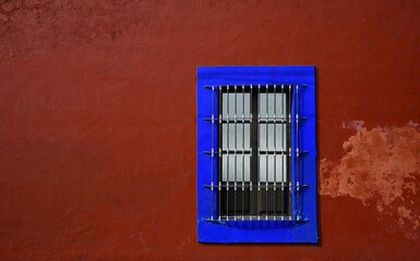 Obraz premium Old traditional Colonial house window with handcrafted wrought iron grilles and an electric blue trim on a Venetian red stucco wall in Cholula, Puebla Mexico. 