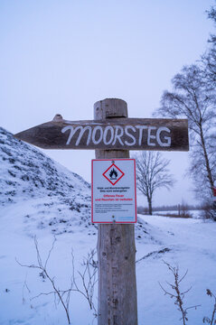 Wooden sign with directional indicator and warning notice in the snowy area, hiking through the snowy moor between Aschen, Diepholz and Lohne, Lower Saxony, Germany