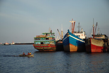 Obraz premium A row of colorful traditional fishing boats moored at the harbor in the afternoon with small boats passing through the calm waters.