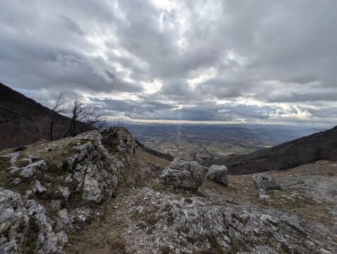 Panorama mozzafiato su una valle montana dall&rsquo;alto di un crinale, con alberi spogli e pendii rocciosi sotto un cielo nuvoloso