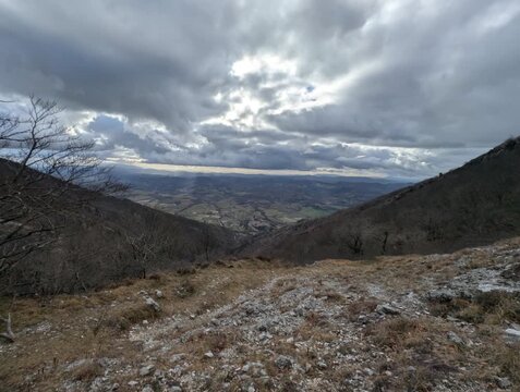 Panorama mozzafiato su una valle montana dall&rsquo;alto di un crinale, con alberi spogli e pendii rocciosi sotto un cielo nuvoloso