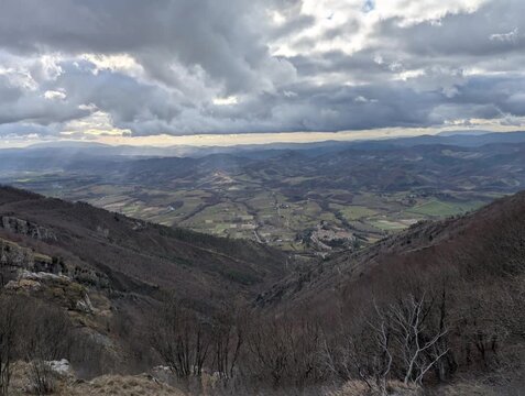 Panorama mozzafiato su una valle montana dall&rsquo;alto di un crinale, con alberi spogli e pendii rocciosi sotto un cielo nuvoloso