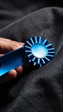 Close-up of a hand holding a blue rosette award against a dark fabric background