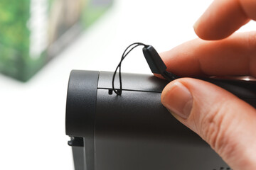 Hand holding a small radio receiver with a connected strap