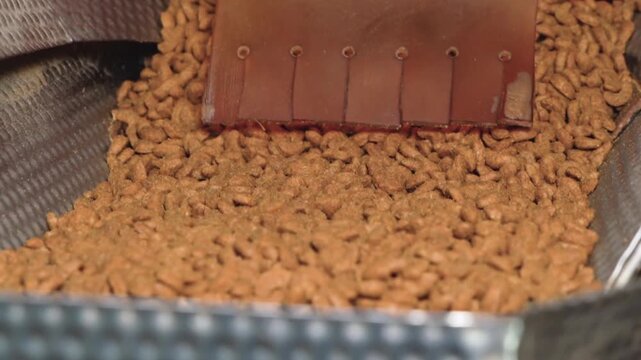 Close up of dry pet food kibble dropping from a manufacturing machine hopper during food production process