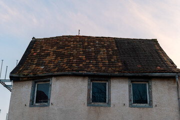 Old wooden roof tiles gleam under the soft evening light of a tranquil sunset sky in a quaint village setting