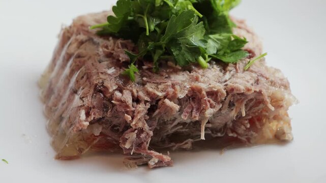 Prepared homemade beef aspic on plate, topping with parsley and dill.