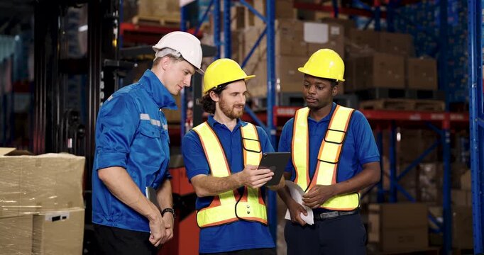 three warehouse workers including caucasian supervisor discussing shipment planning using tablet while standing near cargo pallet teamwork collaboration shown during logistic operation in storage