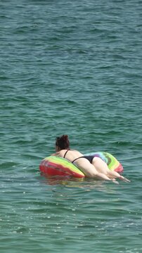 Woman, floating, ocean, relaxing on colorful inflatable float during summer vacation. Vertical video.