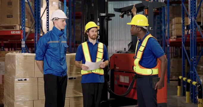 diverse warehouse team of male workers communicating near stacked boxes and forklift with tablet and documents during logistic management discussion inside cargo stock inventory storage facility