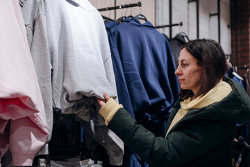 Obraz premium Woman touching a hoodie in a clothing store, evaluating fabric quality.