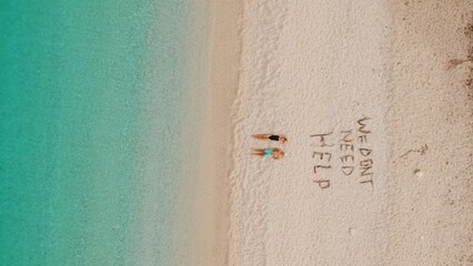 Couple relax on remote turquoise beach beside playful We dont need help sand message. © Olga Gorkun