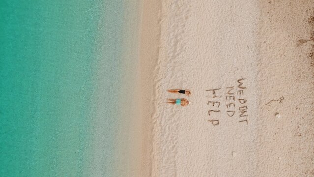Couple relax on remote turquoise beach beside playful We dont need help sand message.