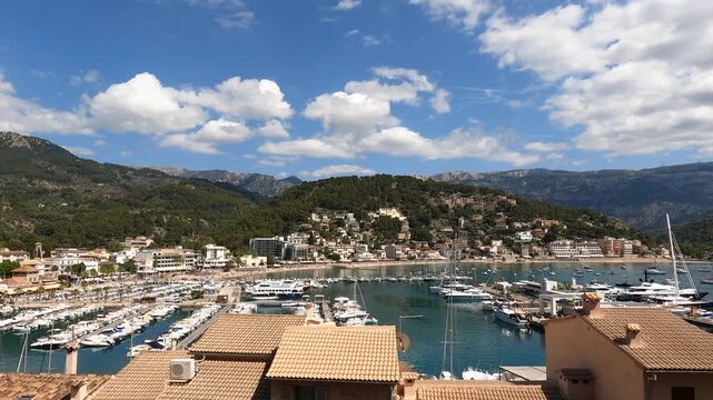 Wide aerial timelapse overlooking the beautiful Port de Soller harbor with luxury yachts, Mediterranean architecture, and scenic mountain backdrop in Majorca.