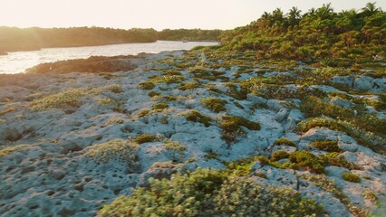 Naklejka premium Woman walking along rocky tropical shore near Grand Sirenis Mexico at sunset.
