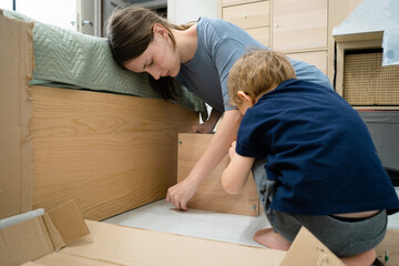 Two children, a teenage girl and a toddler boy, assembling a wardrobe. The little boy is eagerly helping his older sister with the task.
