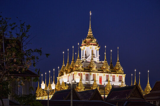 Illuminated Loha Prasat temple at night in Bangkok, showing golden spires and traditional architecture.