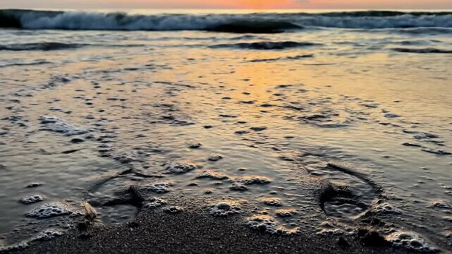 Footprints on the sand at sunset, with waves washing over them.